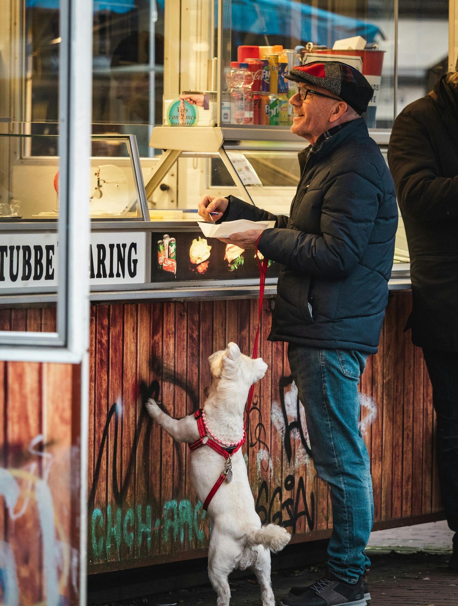 A man and his dog at a street market booth, awaiting an ice cream order.